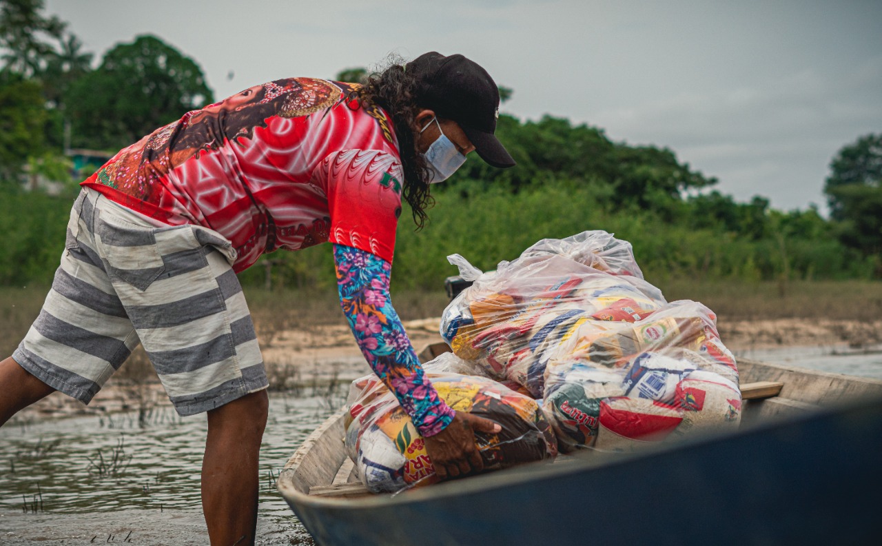 Homem tirando cestas básicas de canoa.