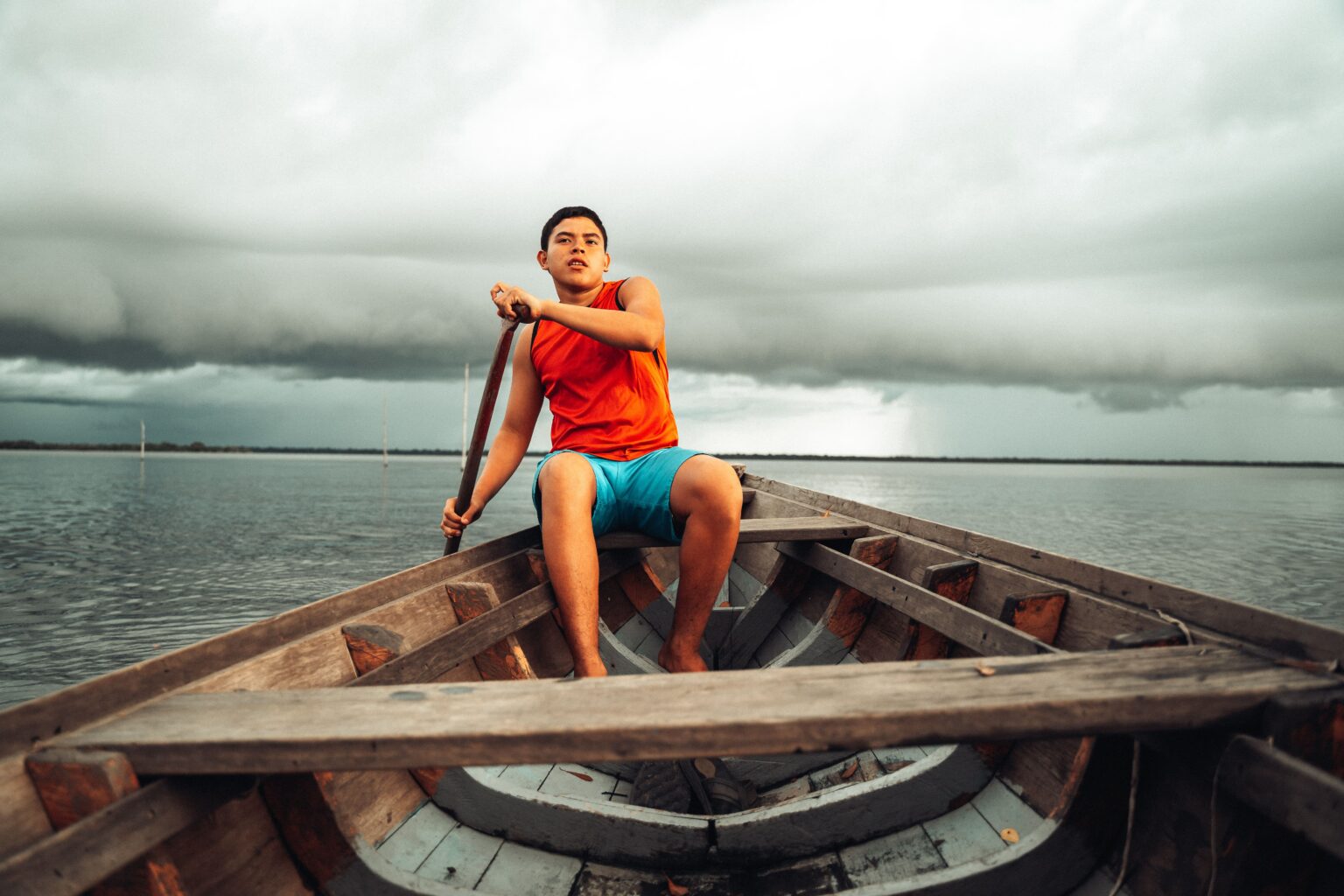 Garoto em canoa remando em meio ao Rio Negro.